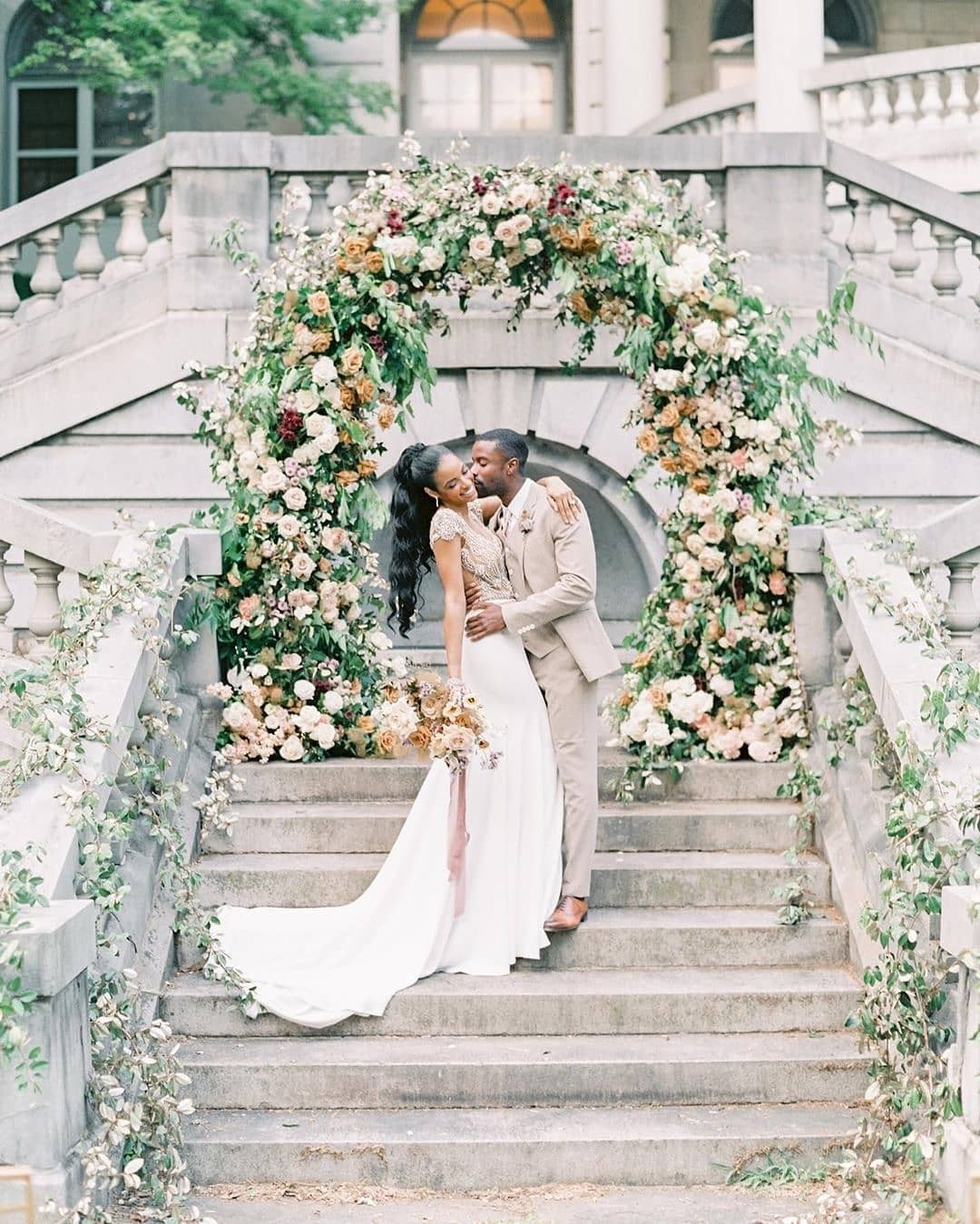 grand staircase with a bride and groom in front of a lush arch with fresh garden flowers
